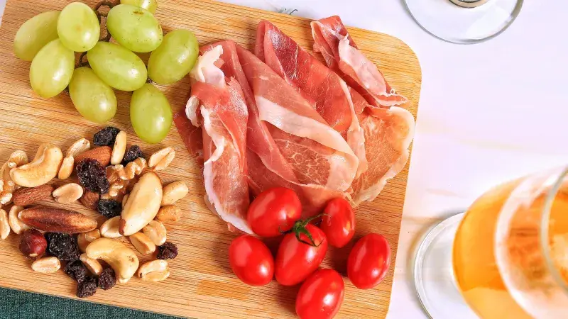 prosciutto, hrozny, cherry rajčata a ořechy na dřevěném prkénku