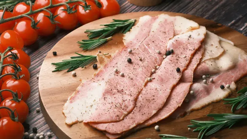 plátky slaniny na prkénku s rozmarínem a cherry rajčaty